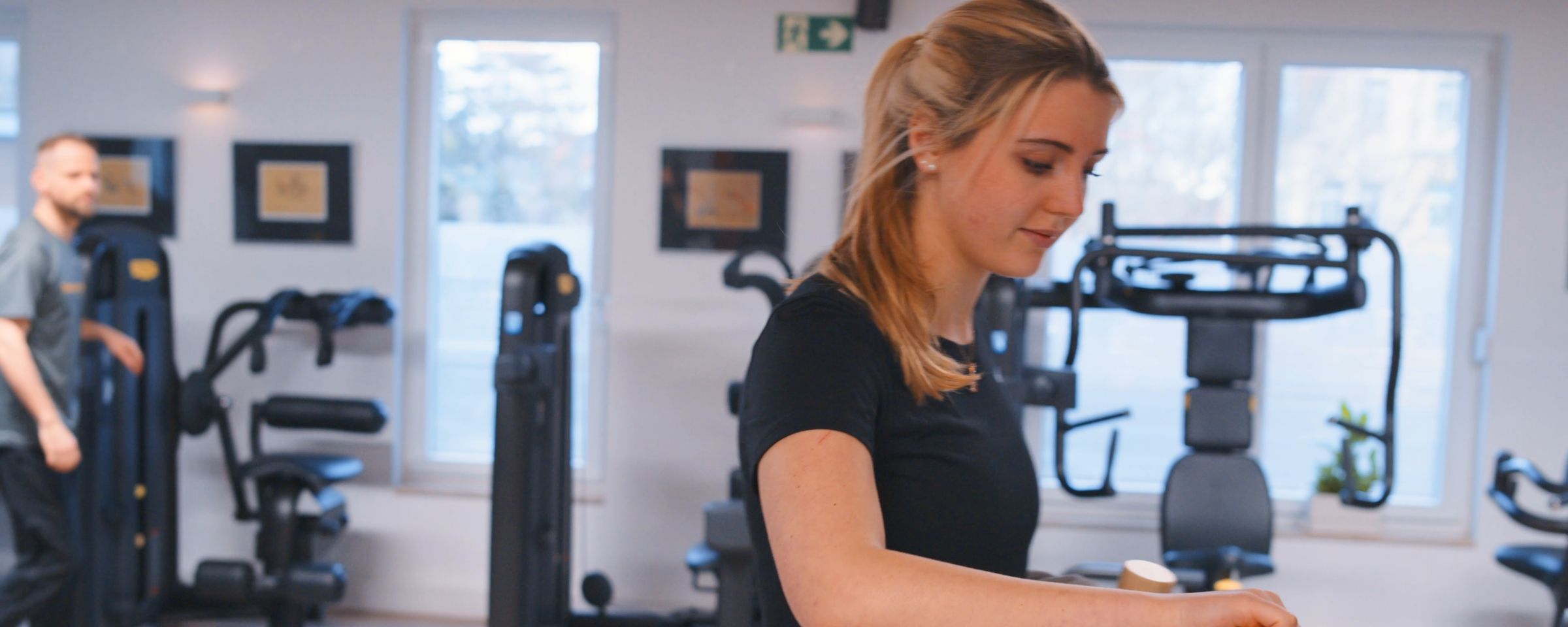 Patientin stellt ein Technogym-Gerät ein, im Hintergrund der Gerätepark