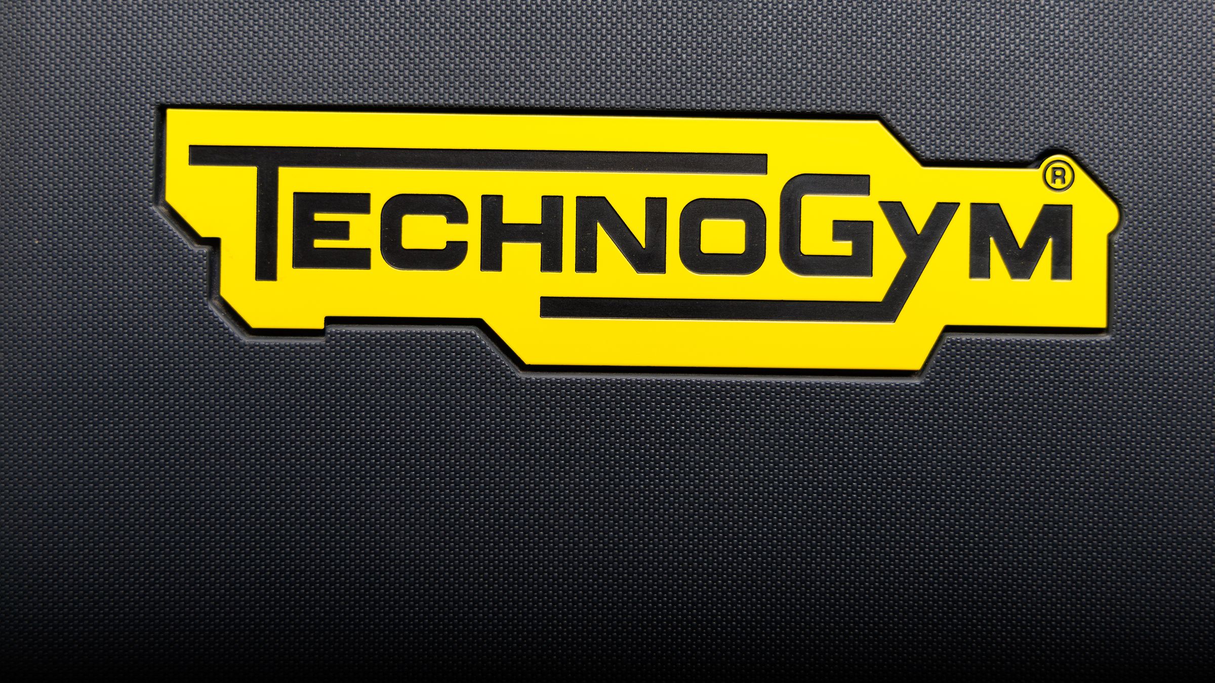 Gelbes Technogym-Logo auf schwarzem Polster eines Trainingsgeräts