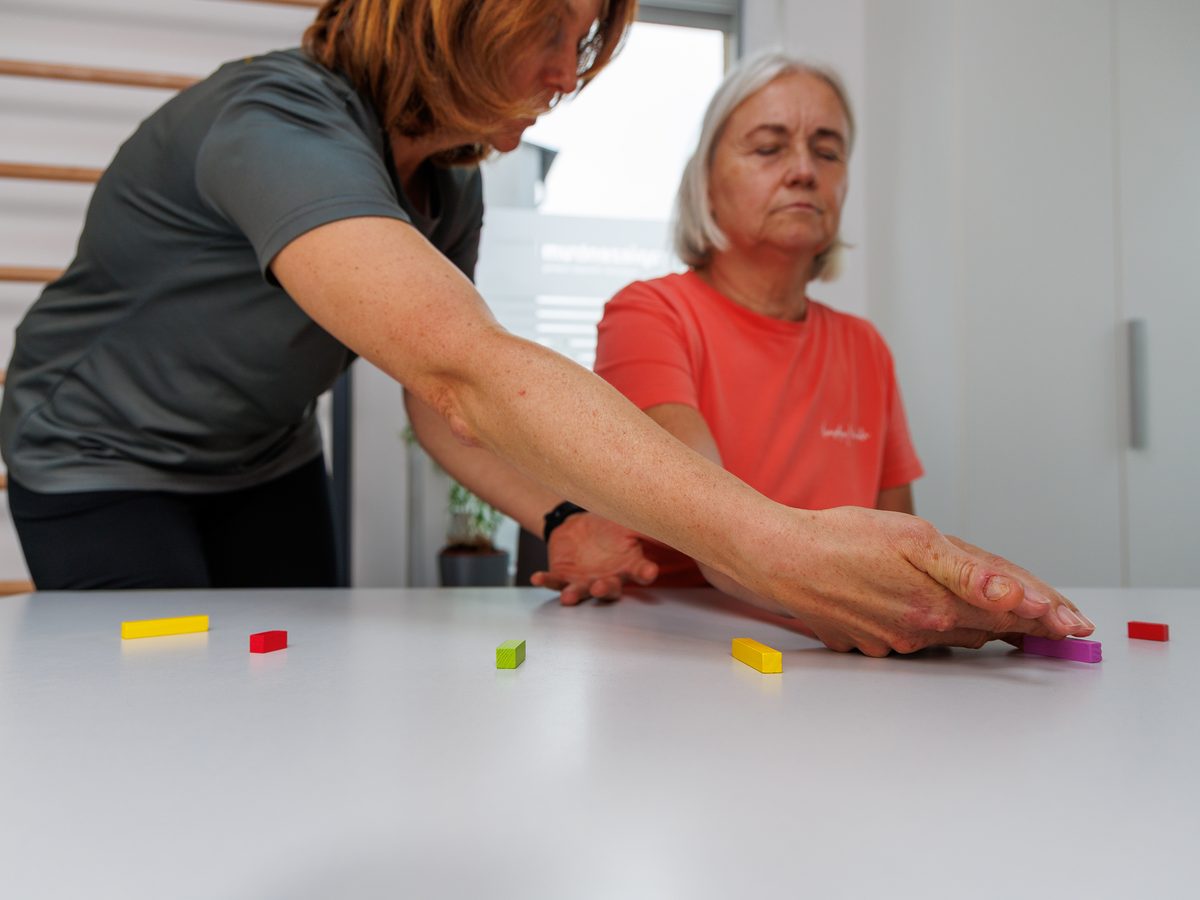 Ergotherapeutin legt einer Patientin am Therapietisch farbige Holzklötze zurecht